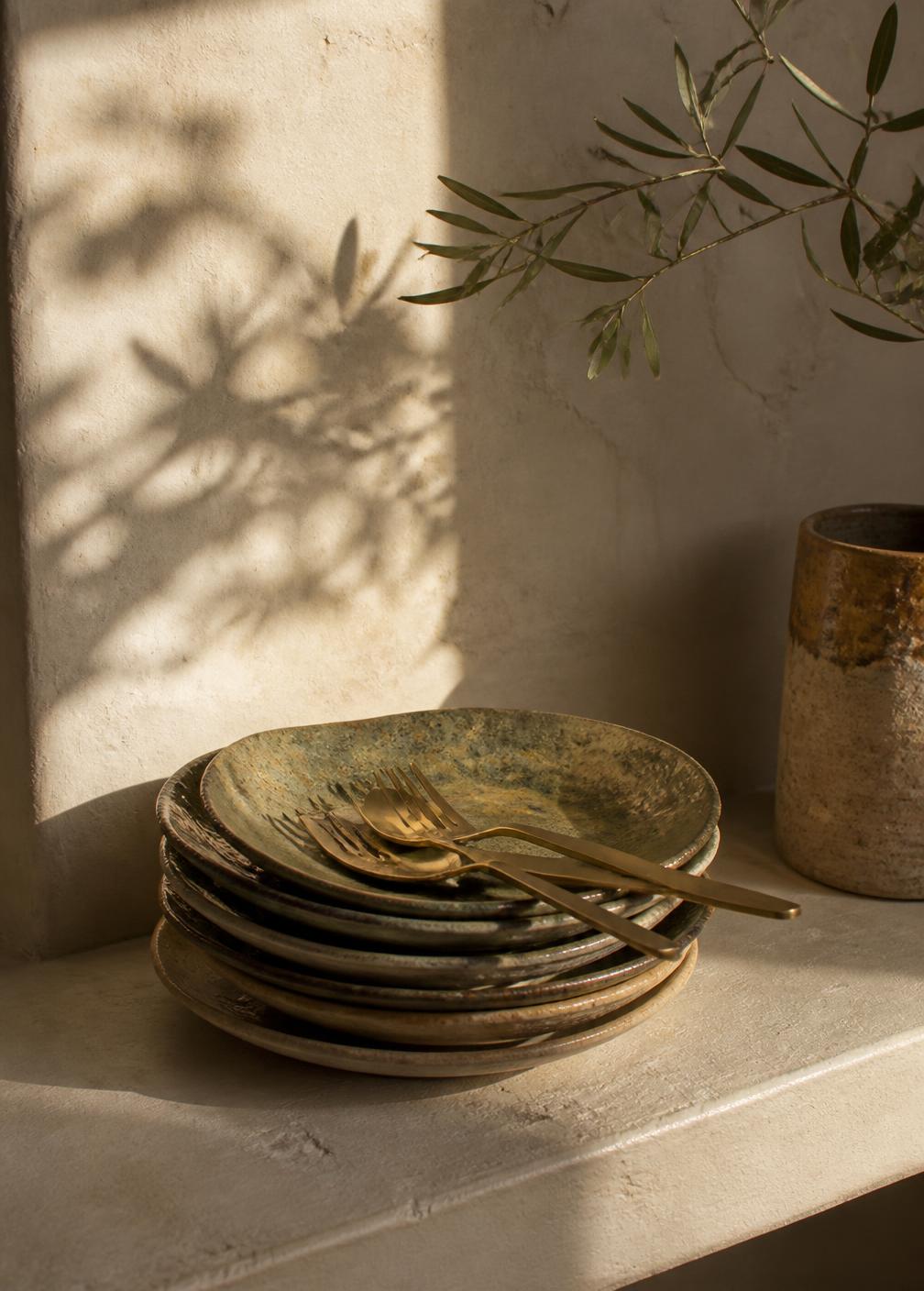 Stacked ceramic plates and brass cutlery in afternoon light