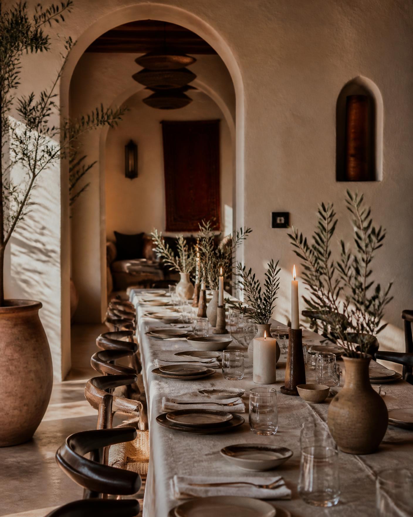 A long table laid with ceramics, linen and olive branches