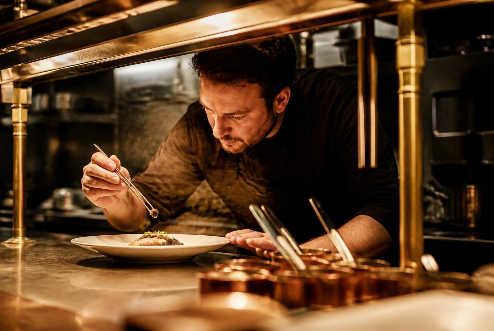 A chef finishing a plate at the kitchen pass